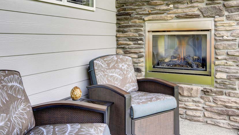 Photo of an outdoor fireplace with stacked stone surround. Two chairs and decorations on the table in the middle.