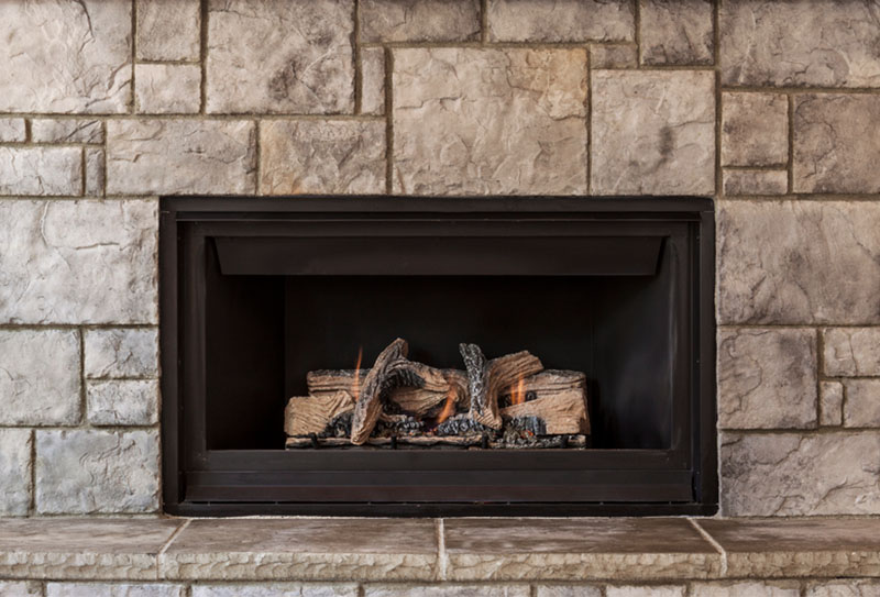 Stock photo of a gas fireplace - Legendary Chimney Solutions A gas fireplace that is lit up with various sized gray stones surrounding it