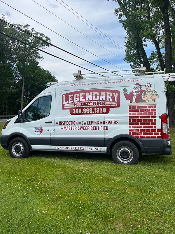 Legendary Chimney Solutions van sitting in grass with electric lines and trees in the background with blue sky and clouds.