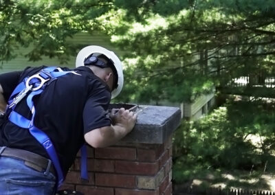 Crew member wearing safety gear inspecting chimney with another home and trees in the background.