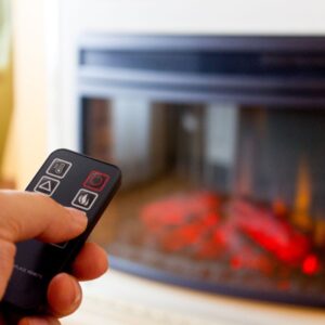 someone turning on a gas fireplace with a remote while enjoying a hot beverage