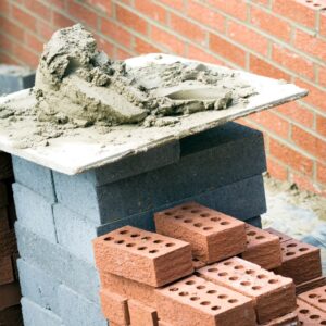 a pile of mortar next to a stack of bricks with a masonry wall in the background
