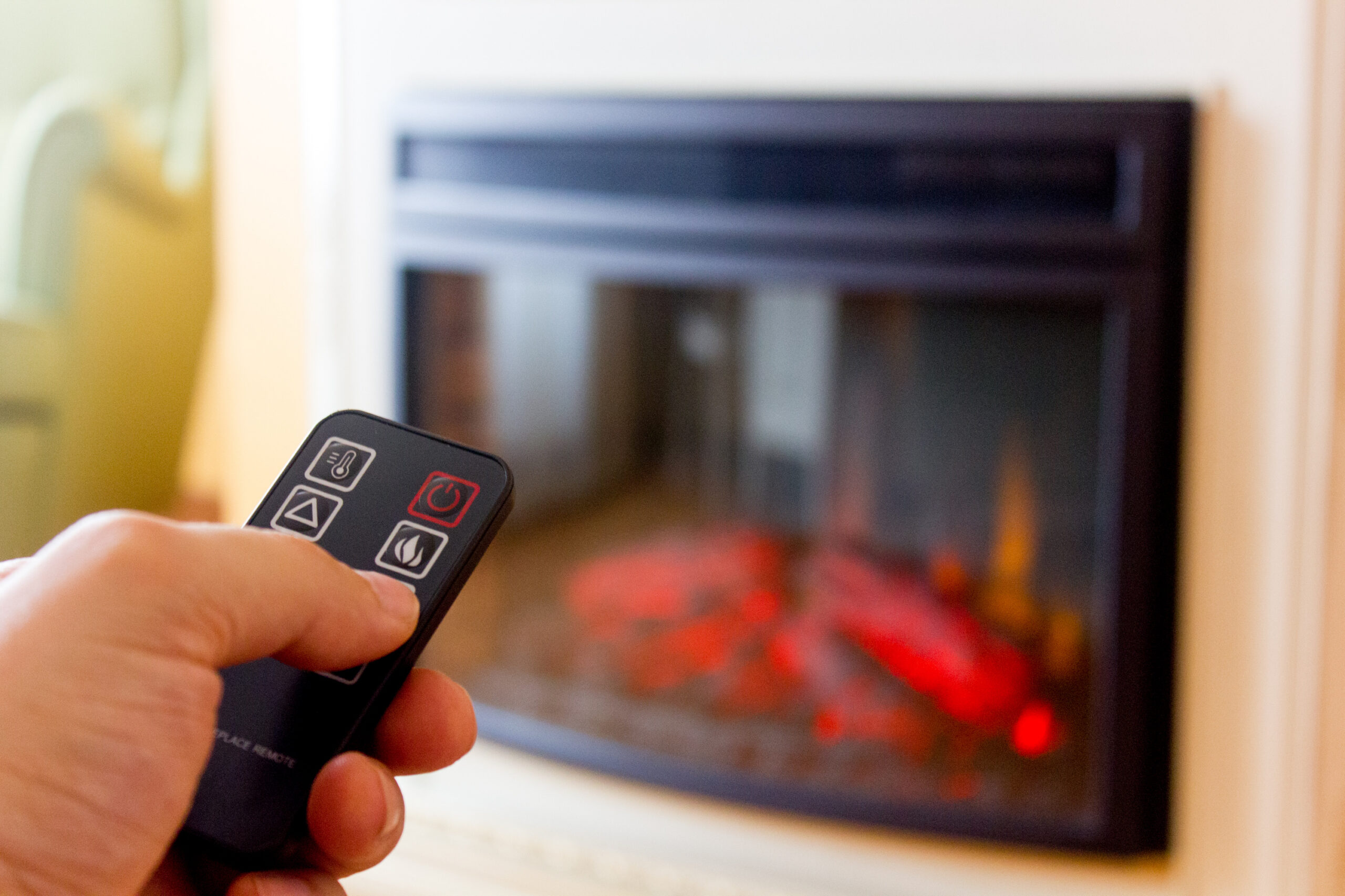 Adobe stock image of someone using a remote to turn on an electric fireplace.